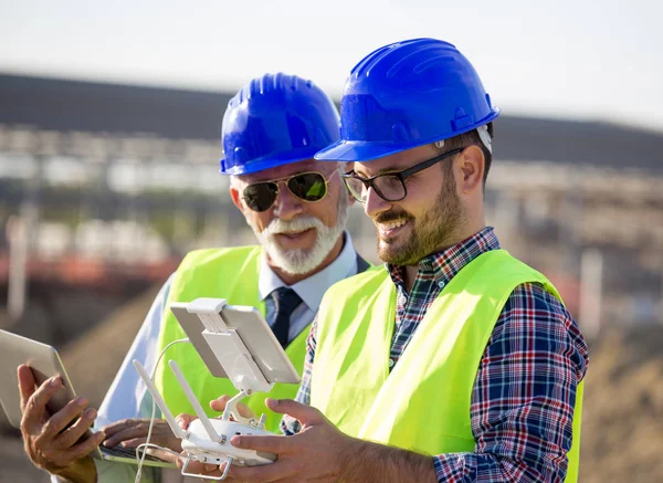 Two engineers with helmets and vests operating with drone by remote control. Technology innovations in construction industry