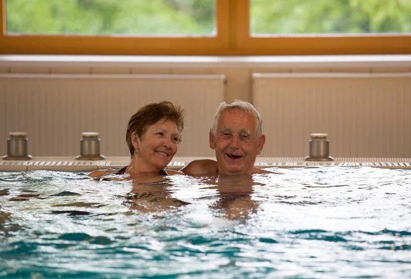 高齢者のカップルをスパ リゾートのお湯で屋内プールで楽しんでください — ストック写真