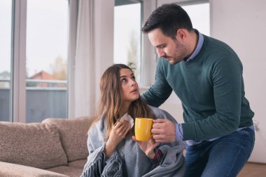 Erkek kız grip olması dikkat çekici. Evde koltukta oturan battaniye ve çay içme ile kaplı