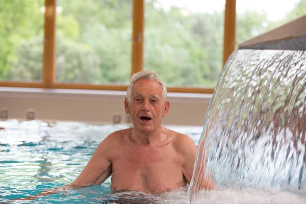 高齢者男温水プールで楽しんで スパリゾートでシャワーをマッサージ — ストック写真