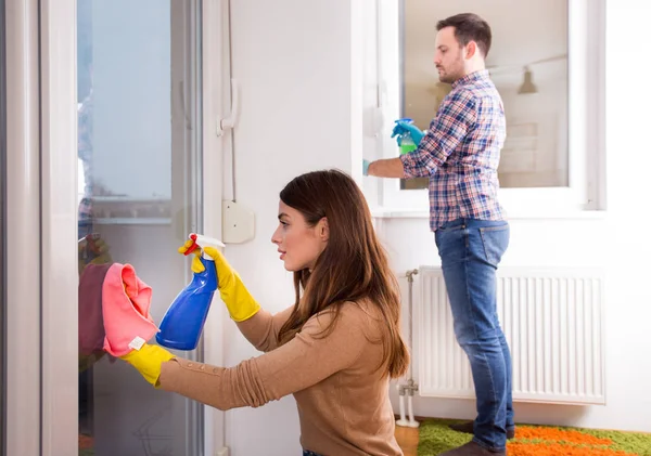 Man and wife cleaning windows with cloth and spray bottle at home