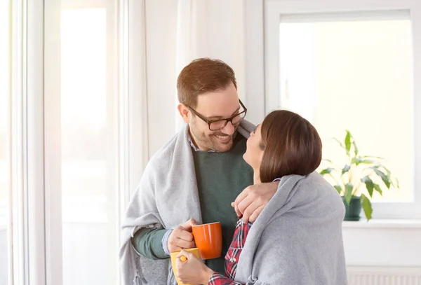 幸福的年轻夫妇在家里的窗户旁拥抱着毯子互相温暖 — 图库照片