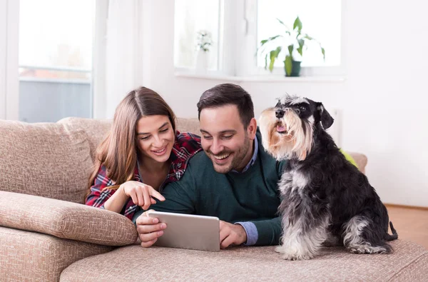 Gelukkige Jonge Paar Liggend Bank Met Hond Kijken Naar Tablet — Stockfoto