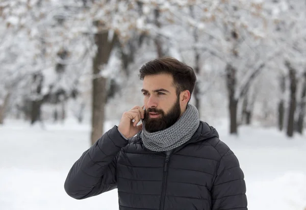 雪と森で携帯電話で話しているひげでハンサムな若い男 — ストック写真