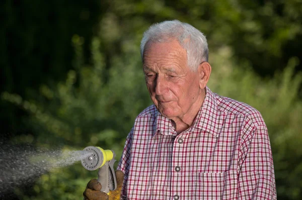 Velho homem regando plantas no jardim — Fotografia de Stock
