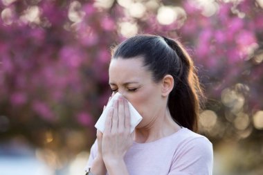 Woman blowing nose because of spring pollen allergy clipart
