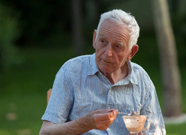 En gammel mann som spiser iskrem i hagen. – stockfoto