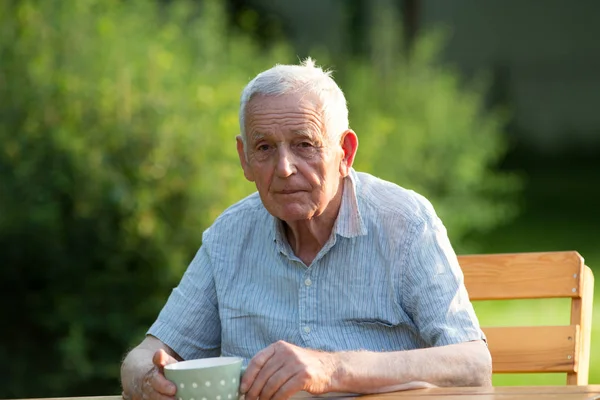 Gammal man dricker te i trädgården — Stockfoto