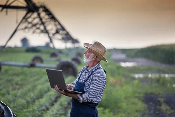 Фермер с ноутбуком перед системой орошения в поле — стоковое фото