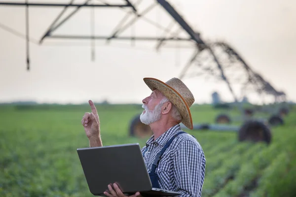 Agricoltore con computer portatile di fronte al sistema di irrigazione in campo — Foto Stock