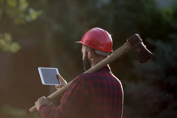 Drwal z siekierą, kask i tablet — Zdjęcie stockowe