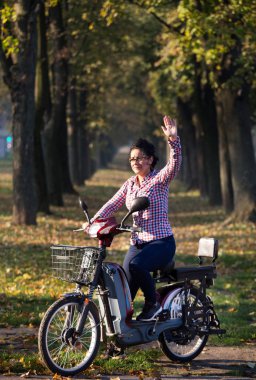 Parkta elektrikli bisiklet süren bir kadın.
