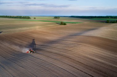Traktörün bahar zamanı gün batımında mısır tohumu ektiği hava görüntüsü.