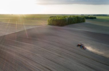 Traktörün bahar zamanı gün batımında mısır tohumu ektiği hava görüntüsü.