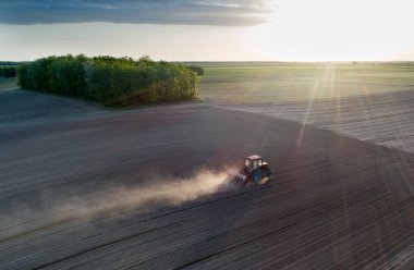 Traktörün bahar zamanı gün batımında mısır tohumu ektiği hava görüntüsü.