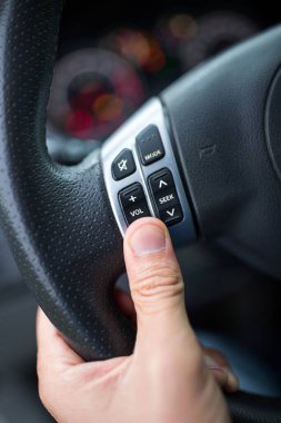 Arabanın direksiyonundaki ses kontrol düğmelerini tutan erkek elini kapat.