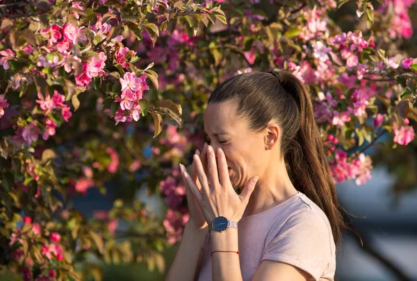 年轻漂亮的女人在开花的树前打喷嚏 春季过敏概念 — 图库照片