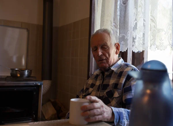 Senior man drinking tea at home in vintage interior of kitchen