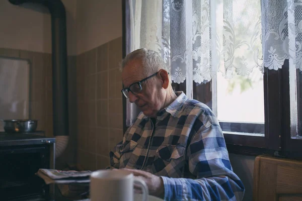 シニア男とともに眼鏡読書新聞でテーブルでヴィンテージインテリアに自宅 — ストック写真