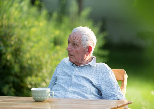 老人坐在花园里 桌上端着一杯茶 — 图库照片