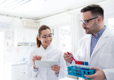 İki doktor test tüplerindeki örnekleri kontrol ediyor ve laboratuardaki tabletlere bakıyor.