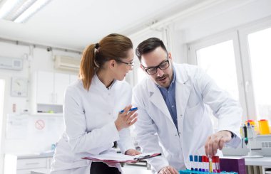 Doktor ve hemşire ellerinde tüp örnekleri tutuyorlar ve laboratuvarda konuşuyorlar.