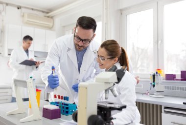 Laboratuvarda test tüpü ve mikroskopla çalışan iki biyolog.