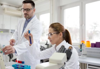 Laboratuvarda test tüpü ve mikroskopla çalışan iki biyolog.