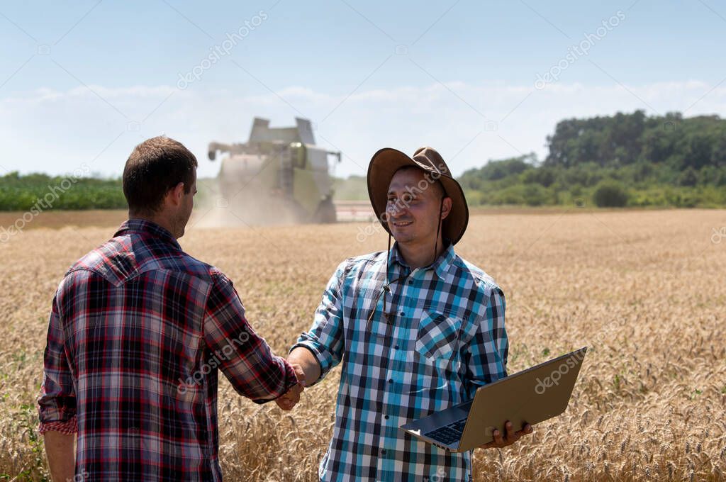 Two farmers shaking hands in wheat field during harvest, with combine harvester in background