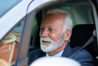 Takım elbiseli yaşlı bir adamın resmi. Araba kullanıyor.