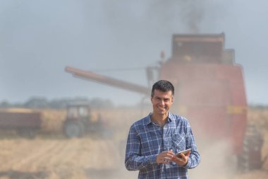 Soya tarlasında duran ve elinde tablet olan yakışıklı çiftçi hasat ve traktörü arka planda çalışan karavanla birleştirdi.