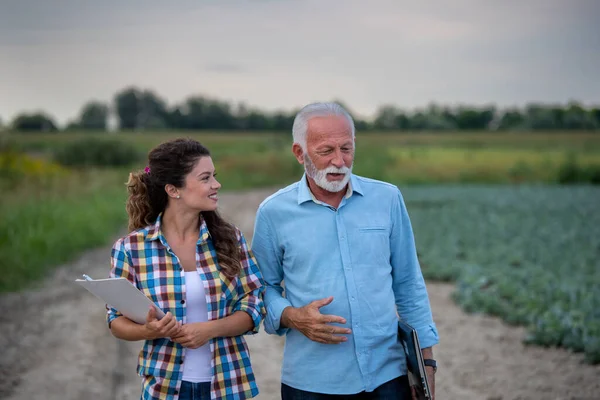 農業の道を歩いて話をする先輩農家と笑顔の若い女性 — ストック写真