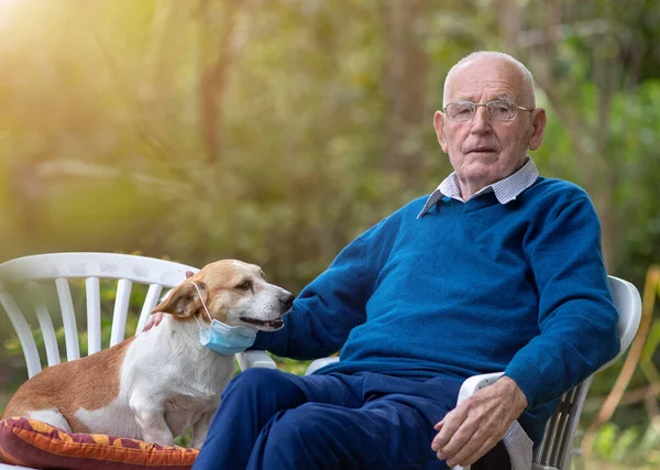 老人坐在花园里 抱着他可爱的狗 戴着防护面具 — 图库照片