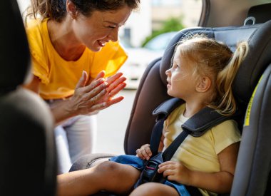 Anne, emniyet kemeriyle bağlanmış bir şekilde araba koltuğunda oturan genç kızıyla samimi bir şekilde yakınlaşıyor.