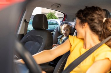 Küçük kız aptalca surat asıyor ve arka koltuktan elini uzatıyor. Annesi de onu arabanın koltuğundan kontrol ediyor.