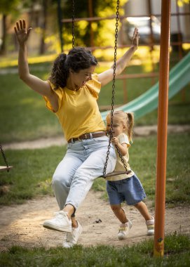 Neşeli bir çocuk, neşeli bir parkta salıncakta annesine doğru koşuyor, kahkaha ve oyunla dolu neşeli bir öğleden sonra geçiriyor..