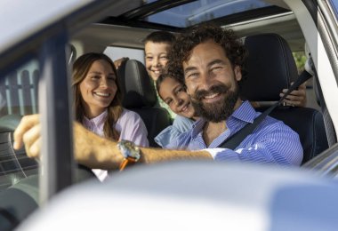 İki çocuklu neşeli bir aile, keyifli yolculukları sırasında arabalarıyla mutlu bir şekilde seyahat eder, gülümsemelerini ve kahkahalarını paylaşırlar.
