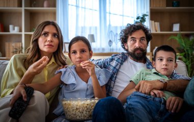 Dört kişilik aile kanepede oturup patlamış mısırlı film izliyor. Meşgul ve odaklanmış görünüyorlar, birlikte vakit geçirmekten zevk alıyorlar.