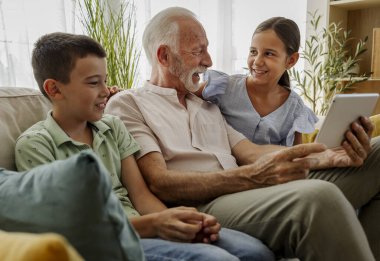 Büyükbaba, torunlarına tablette bir şey gösterirken onlarla eğlenmeyi sever. Sıcak oturma odası kahkahalarla dolu.