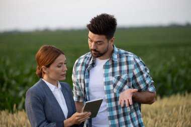 Çiftçi ve iş kadını, ciddi tartışmalar yaparken dijital tablet kullanarak tarlada duruyorlar.