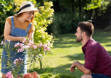 Bahçede çiçeklerle ilgilenen genç bir kadın. Yanında çömelmiş bir adam var ve işine hayran.