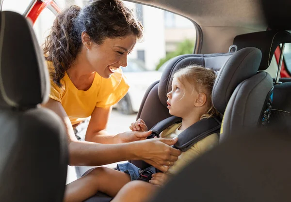 Sevimli kızını emniyet koltuğuna oturturken gülümseyen özenli genç bir anne. Parka gitmek için araba yolculuğuna hazırlanıyorum. 