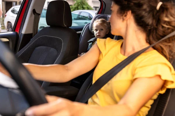 Anne, güneşli bir günde arka koltukta otururken, sürücü koltuğunda otururken arkasına bakıyor.