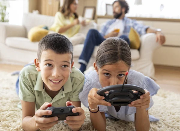 Yetişkinler kanepede dinlenirken iki çocuk halıda video oyunu oynuyor. Nişanlandılar ve eğleniyorlar.