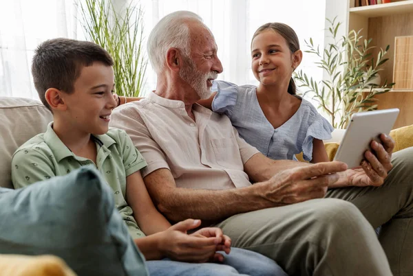 Büyükbaba, torunlarına tablette bir şey gösterirken onlarla eğlenmeyi sever. Sıcak oturma odası kahkahalarla dolu.