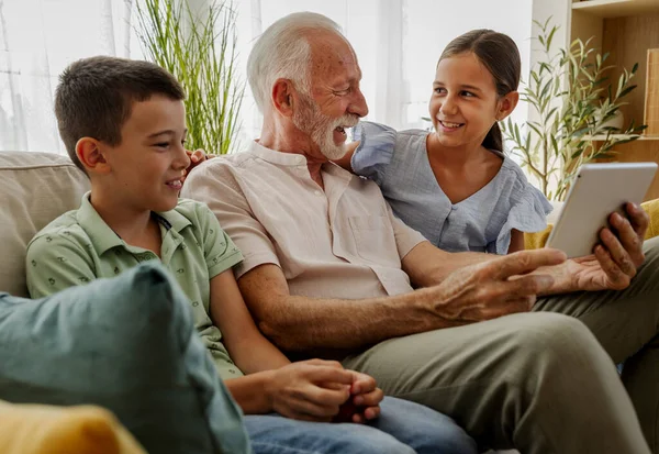 Büyükbaba, torunlarına tablette bir şey gösterirken onlarla eğlenmeyi sever. Sıcak oturma odası kahkahalarla dolu.