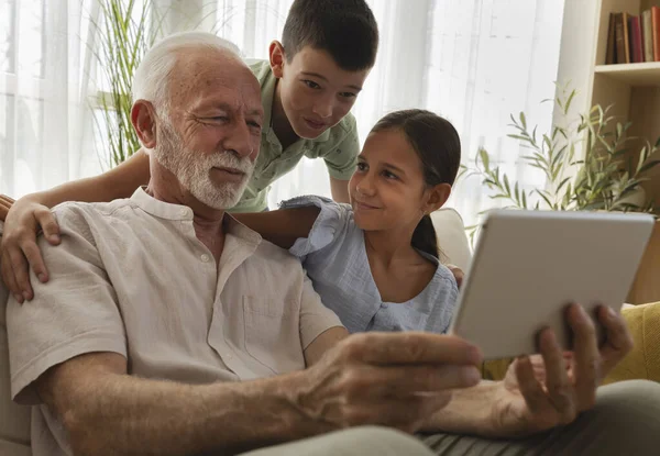Büyükbaba, kız ve oğlanlarla vakit geçirmeyi seviyor. Tablete bakıp gülümsüyor. Parlak, davetkar bir oturma odasında.