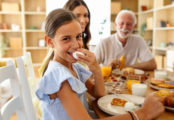 Masadaki diğer kızlar gülümserken bir kız yumurta yiyor. Lezzetli kahvaltı öğeleri onları sıcak bir yemek alanında kuşatır..