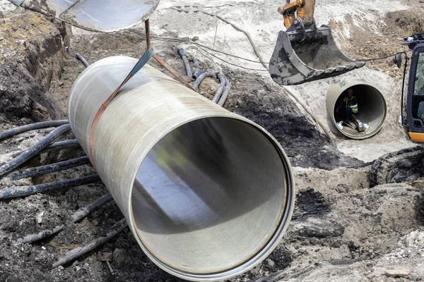 Excavator bucket lifting very large underground pipe — Stock Photo, Image