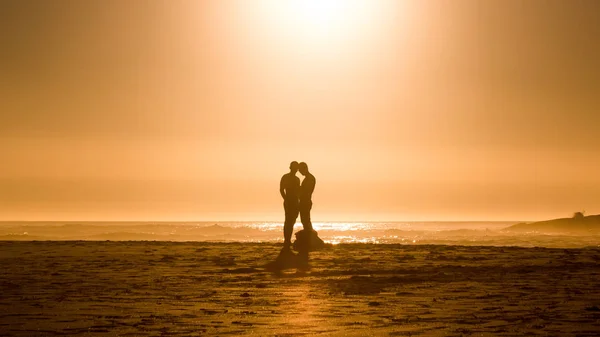 Orange sunset silhouette male couple on beach in Cape Town, South Africa